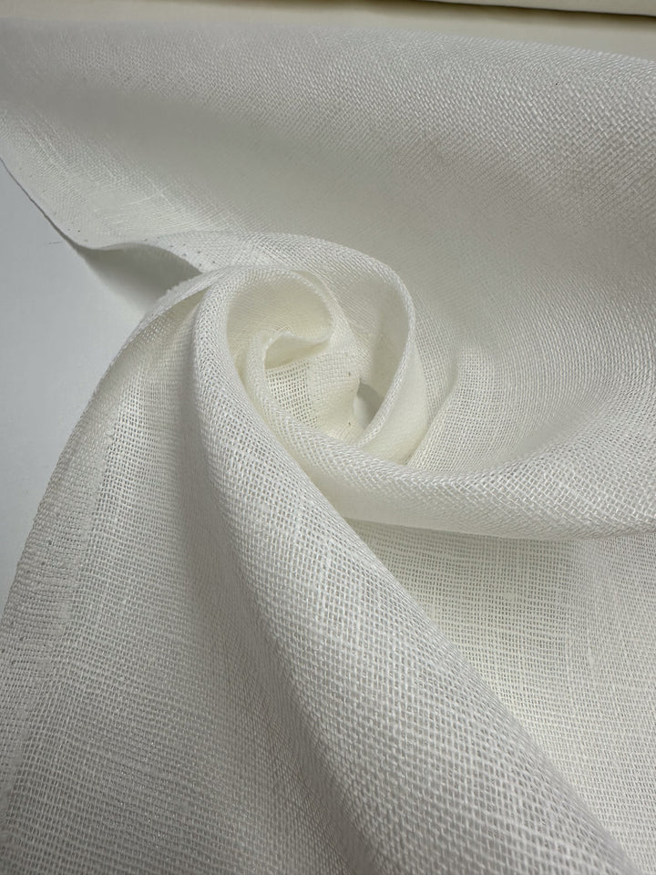 Super Cheap Fabrics' Loose Weave Pure Linen - Off White (150cm) is displayed draped and swirled, showcasing its breathable, lightweight texture and semi-transparent, open weave.