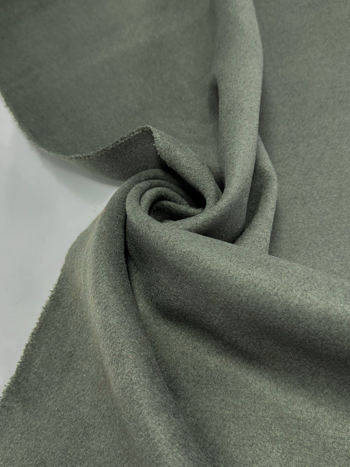 A close-up of Super Cheap Fabrics' Wool Cashmere - Agave Green - 150cm, showing its luxurious, slightly fuzzy texture spiraled on a flat surface to highlight the premium softness.