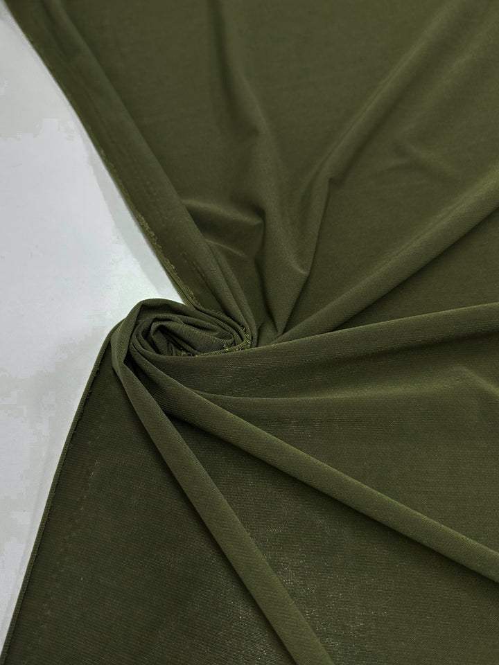 The Super Cheap Fabrics ITY Knit - Olive Green - 150cm is laid flat with a corner twisted into a spiral, highlighting its smooth texture and soft folds against a white background.
