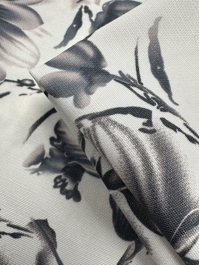Close-up of folded Designer Deadstock - Inkveil - 145cm from Super Cheap Fabrics featuring a black and gray floral pattern on light viscose, showing textured details. Ideal for unique ex-designer projects.
