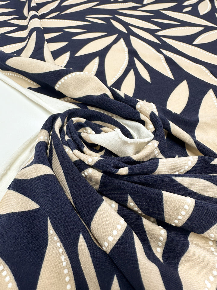 A close-up of Super Cheap Fabrics' Textured Lycra - Prism Leaf (150cm), a medium-weight Polyester/Spandex with a navy and beige large floral pattern featuring dotted outlines, shown swirled on a white surface.