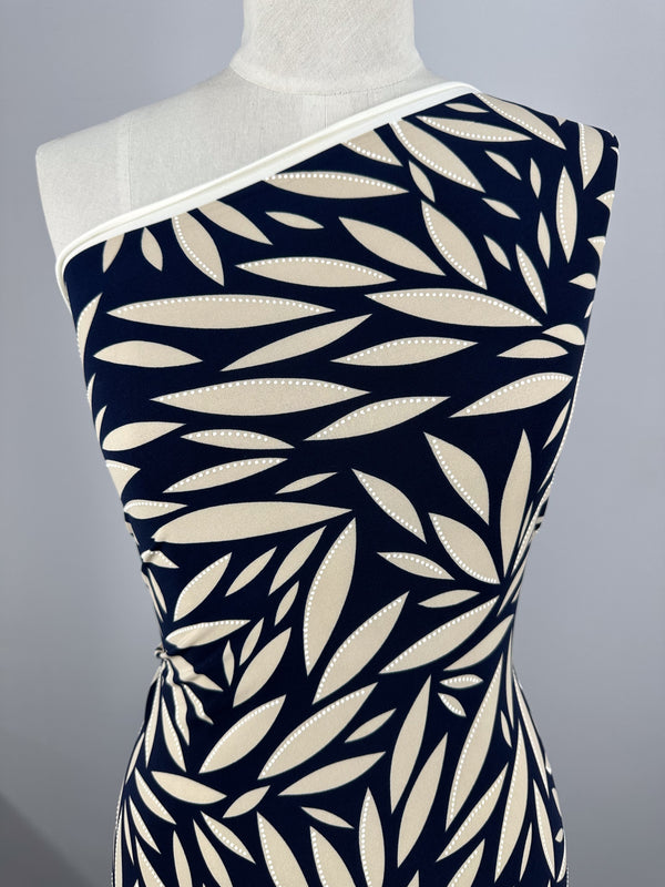 A mannequin wears a fitted one-shoulder dress made from Super Cheap Fabrics' Textured Lycra - Prism Leaf (150cm), showcasing a bold navy and beige leaf design with white dotted outlines and white trim at the neckline.