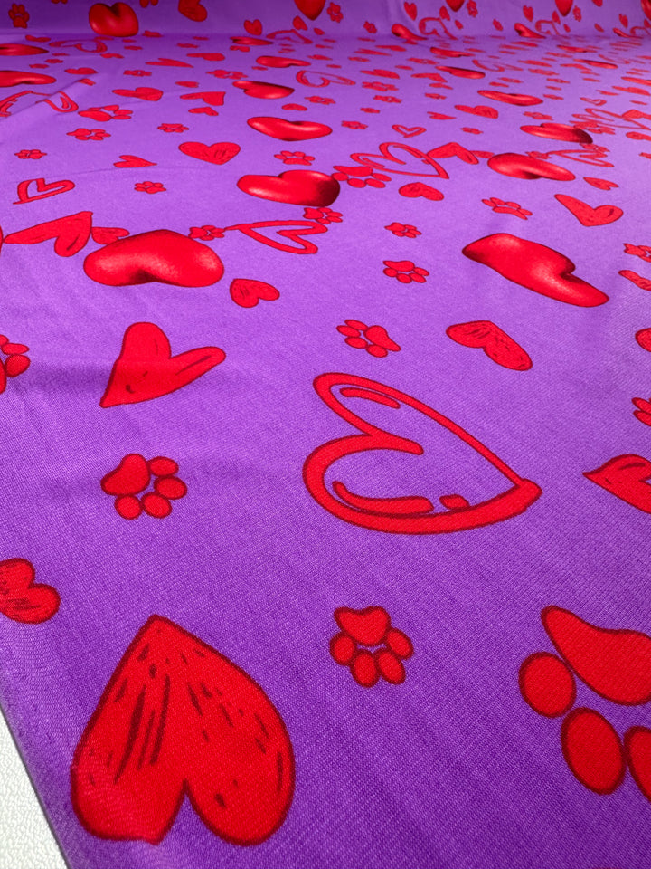 Printed Lycra - Love Riot - 150cm by Super Cheap Fabrics features red hearts and playful paw prints on purple, creating a vibrant, lively pattern—perfect for bold, eye-catching projects.