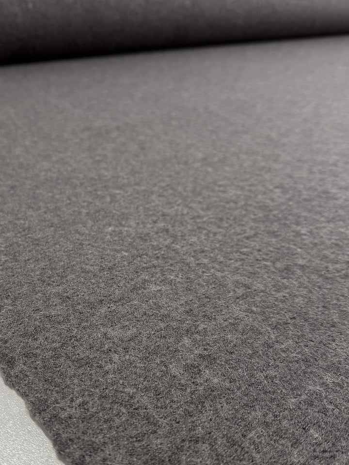 Close-up of Super Cheap Fabrics' Boiled Wool - Ghost Gray (145cm): a soft, textured felt fabric unrolled on a smooth surface, perfect for making cozy winter garments.