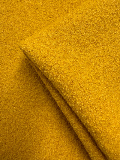 A close-up of Boiled Wool - Mango Mojito (150cm) from Super Cheap Fabrics shows its vibrant yellow, heavy weight texture, neatly folded at the corner with a soft, slightly fuzzy surface.