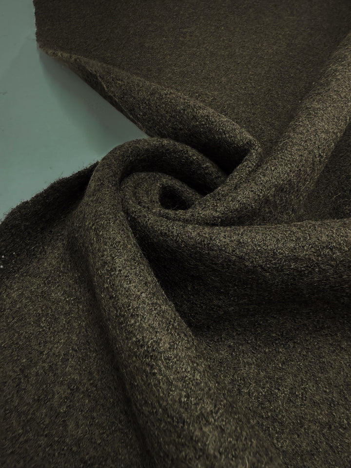 A close-up of Boiled Wool - Forest Night (152cm) by Super Cheap Fabrics, spread out and loosely twisted into a spiral on a light surface—ideal for crafting cozy winter garments.