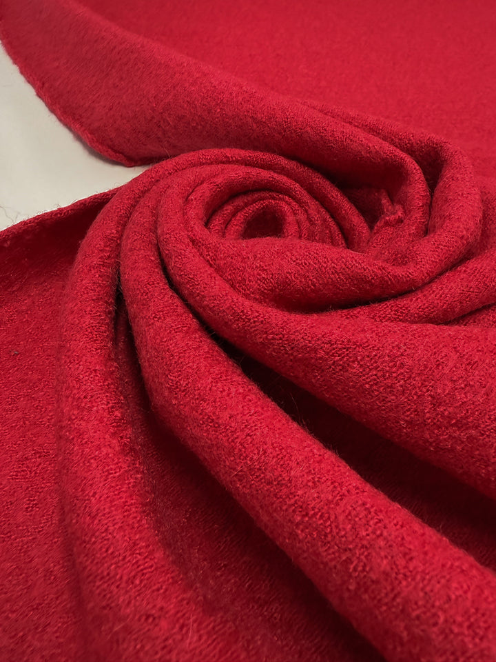 A close-up of Super Cheap Fabrics' Boiled Wool - Crimson - 145cm, partially unrolled to reveal its soft, fuzzy texture and thick, heavyweight material in a vivid red shade.
