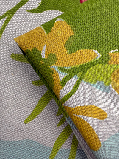 A close-up of Super Cheap Fabrics’ Pure Linen - Garden Reverie - 150cm, featuring a floral print in yellow, green, and white, folded neatly on a gray and blue textured surface—perfect for vibrant projects.