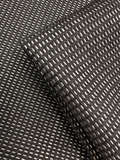 A close-up of Super Cheap Fabrics' Linen Blend - Silver Dash (135cm) highlights its grid pattern of raised, shiny rectangles, with one luxurious piece draped diagonally over another—ideal for sophisticated upholstery projects.