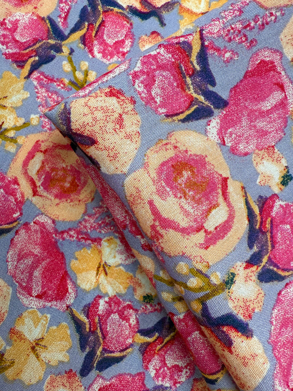 A close-up of Designer Rayon - Botanic Crush by Super Cheap Fabrics, featuring a colorful floral pattern with large pink, yellow, and cream flowers and green leaves on a light blue background—ideal for vibrant prints.