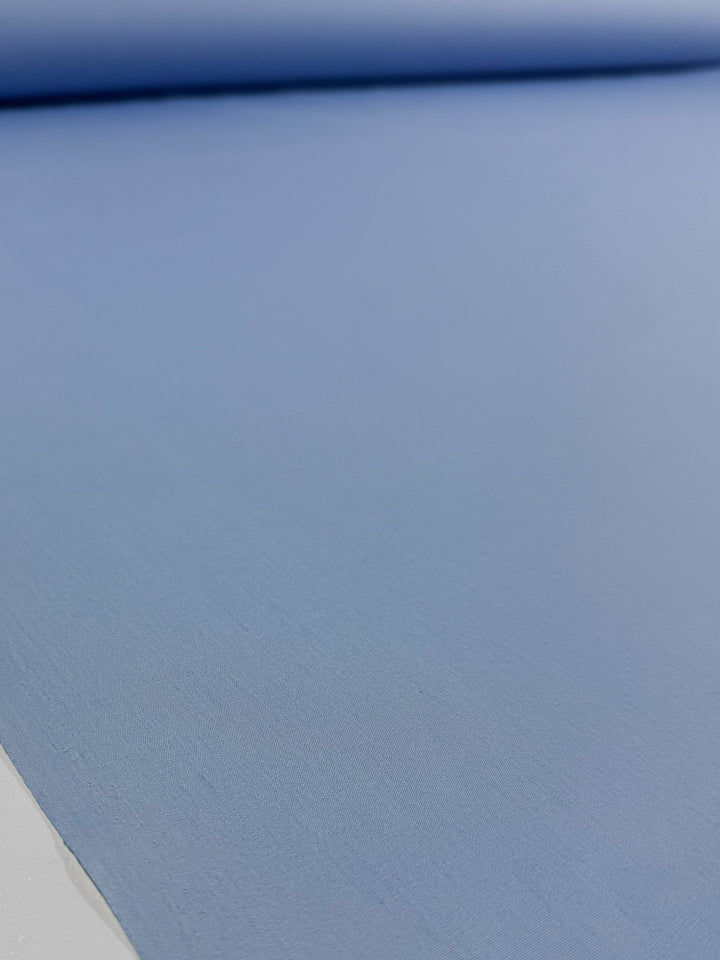 A close-up of Super Cheap Fabrics' Poplin - Powder Blue - 114cm shows the smooth, even texture of this lightweight poly cotton fabric, laid flat with a matching roll in the background.