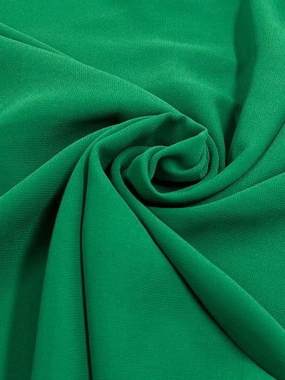 A close-up of the Hi-Multi Chiffon - First Tee fabric from Super Cheap Fabrics, featuring a spiral pattern in green. The lightweight material has a smooth and soft feel with a subtle texture. The dynamic folds create a swirling design at the center, reminiscent of floaty tops.