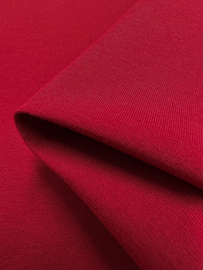 A close-up of folded Cotton Lycra - Karanda Red by Super Cheap Fabrics showcases its smooth, woven texture. Light enhances the rich color and fine details of this medium-heavy 165cm fabric.
