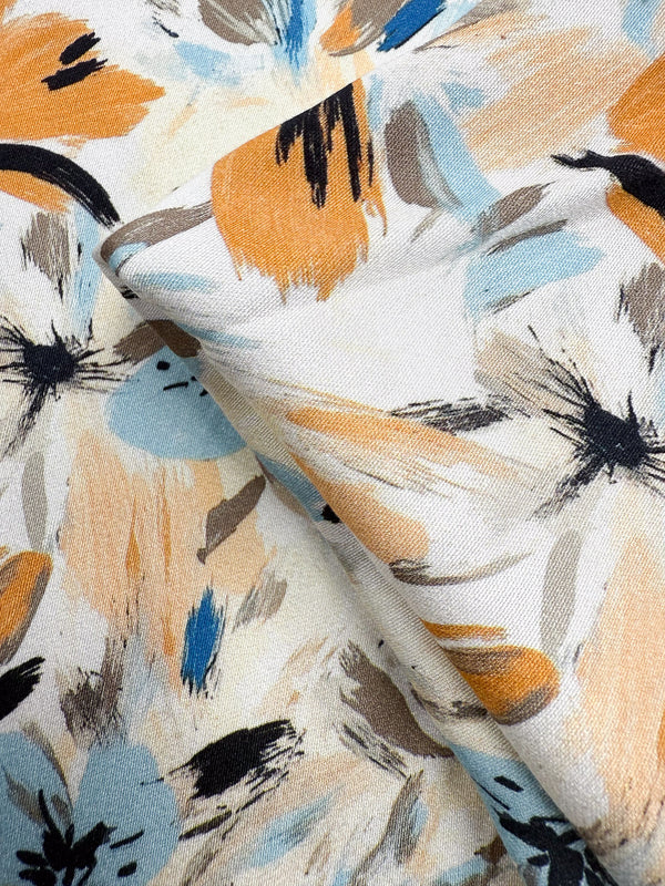 A close-up of Super Cheap Fabrics' Mercerised Rayon - Autumn Haze (150cm), featuring lightweight, breathable fabric with overlapping abstract floral brushstrokes in beige, light blue, black, brown, and orange.