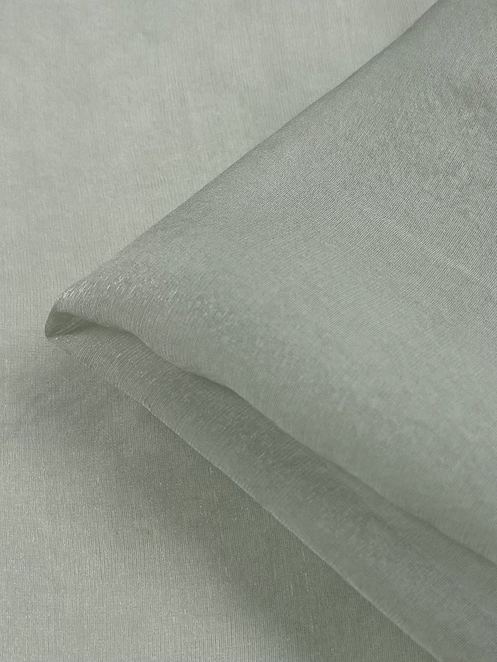 Close-up image of folded Silk Mousseline - Frost by Super Cheap Fabrics, showcasing light green fabric with a subtle sheen, metallic shimmer, smooth texture, and fine weaving pattern. Width: 140cm.