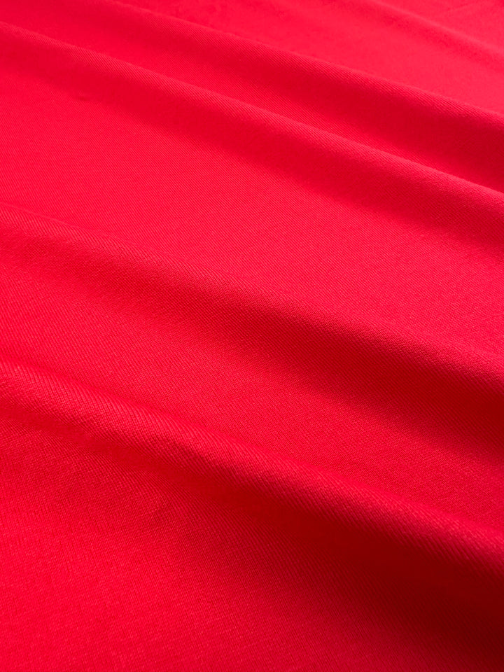 Close-up of smooth Ribbon Red Cotton Jersey by Super Cheap Fabrics, 165cm wide, with diagonal folds creating soft shadows and highlights. The fine texture appears slightly shiny, suggesting a silky or satin-like look.