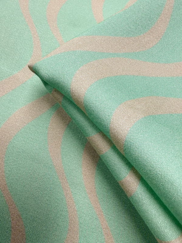 A close-up of Super Cheap Fabrics’ Mercerised Rayon - Seafoam Rhythm (150cm) shows its smooth, lightweight texture and modern seafoam-green fabric with beige abstract wavy lines.