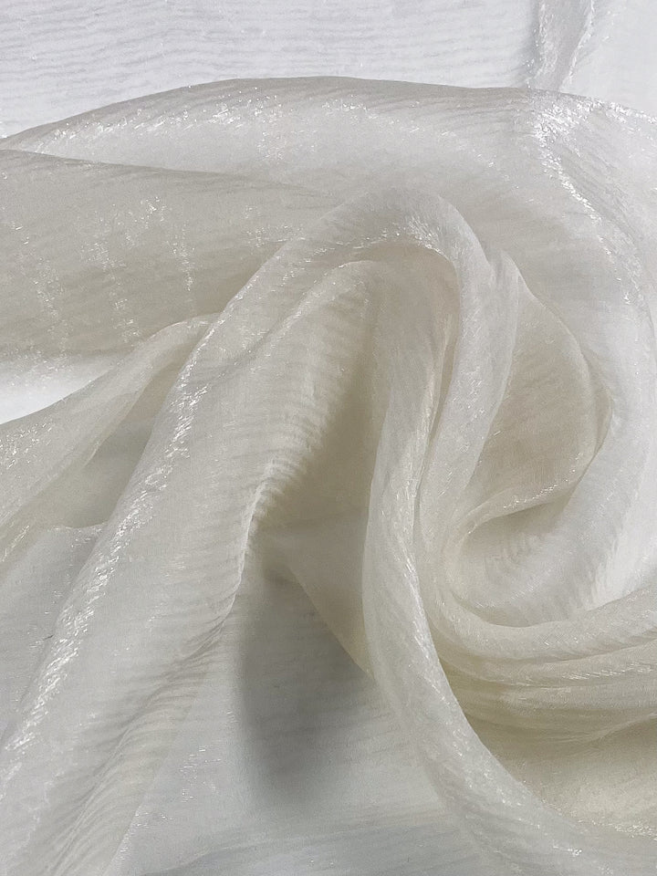 Close-up of Super Cheap Fabrics' Silk Mousseline in Milk, 137cm wide, featuring a translucent textured white fabric with soft folds and a subtle metallic shimmer that highlights its delicate silky appearance.
