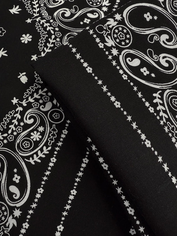 Close-up of Designer Rayon - Bandana Noir (148cm) by Super Cheap Fabrics: black lightweight rayon with a white paisley and floral bandana pattern, featuring intricate swirls, flowers, and dotted lines.