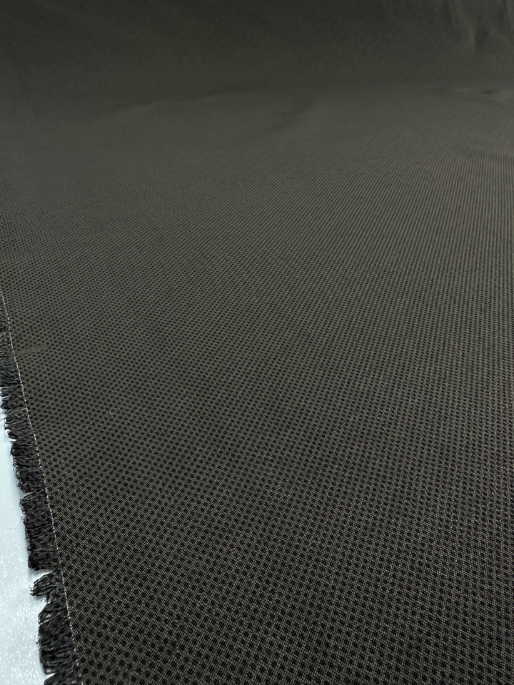 Close-up of Printed Bengaline - Pin Dot Khaki fabric by Super Cheap Fabrics. It's dark green, medium-weight, with a small diamond pattern. The structured woven texture extends flat beyond the frame, and slightly frayed edges add character. Width: 150cm.
