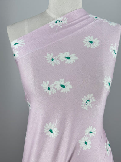 The mannequin showcases Super Cheap Fabrics' Printed Cotton Lycra in Daisy Pink, featuring white daisies with green centers on light purple fabric. The medium-weight lycra elegantly drapes over one shoulder against a gray background. Width: 150cm.