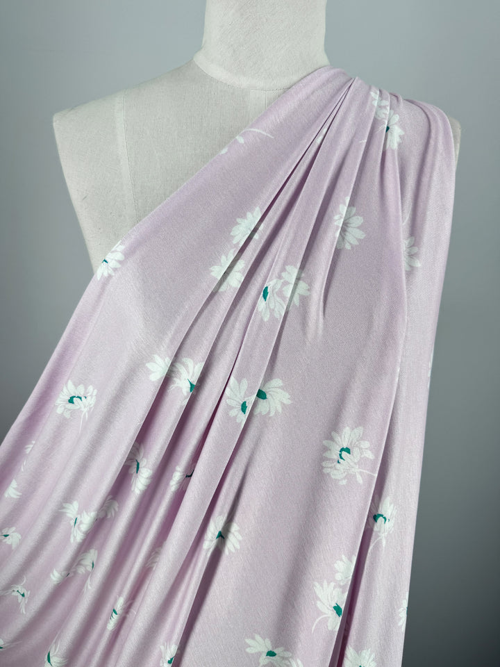 The mannequin is draped with Super Cheap Fabrics' Printed Cotton Lycra - Daisy Pink (150cm), featuring pale pink fabric adorned with white daisies and green centers. This medium-weight Lycra gathers elegantly over the shoulder, highlighting its soft texture and floral design.