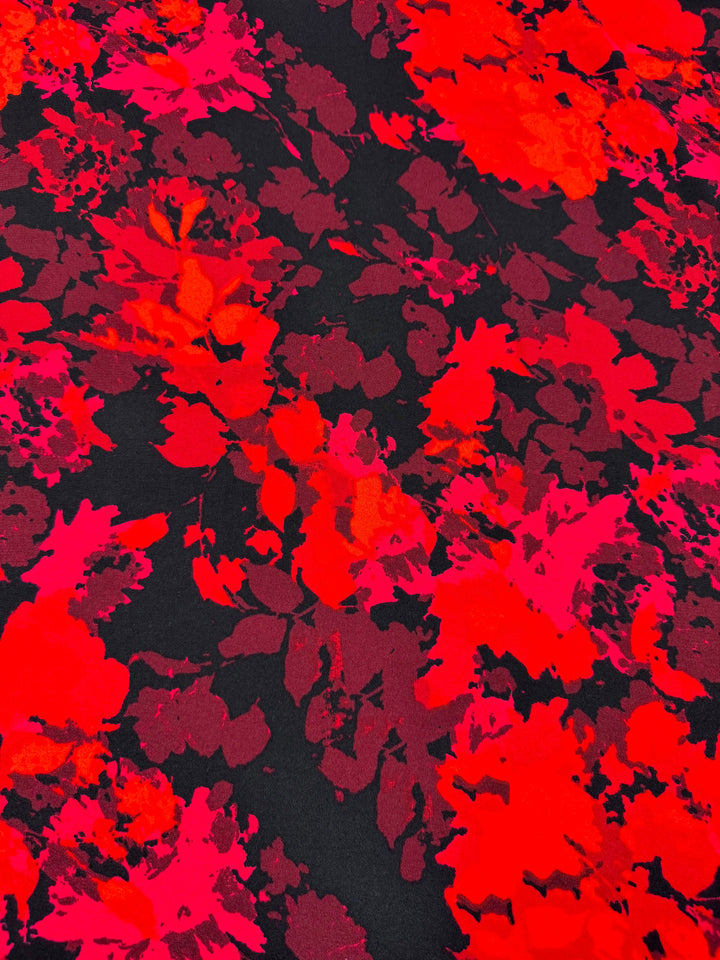 The Printed Crepe - Burn by Super Cheap Fabrics features a vivid floral pattern with bright red and pink flowers on a dark background, creating a dynamic and vibrant texture that's perfect for fashion garments.