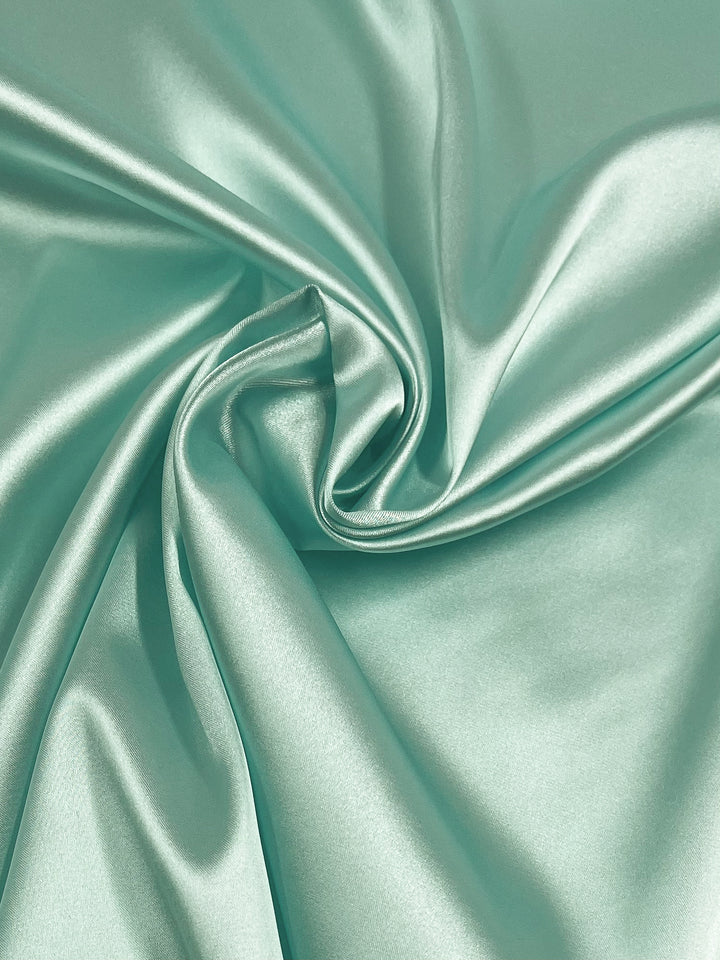A close-up of Satin Deluxe - Mint by Super Cheap Fabrics, a smooth, shiny 150cm-wide dressmaking fabric with soft folds and swirling patterns in lightweight polyester.
