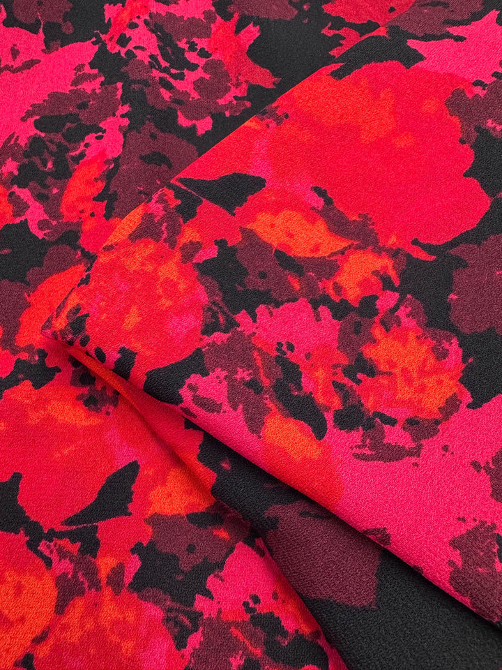 A close-up of Super Cheap Fabrics' Printed Crepe - Burn - 150cm reveals vibrant red, pink, and black floral patterns. Its smooth texture enhances fashion garments with a bold, artistic design.