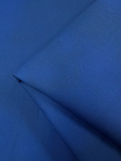 A close-up of the Royal Cotton Drill from Super Cheap Fabrics displays its dense weave and rich deep blue hue. The fabric's smooth and textured surface creates subtle shadows in the folds, enhancing its vibrant color. Width: 148cm.