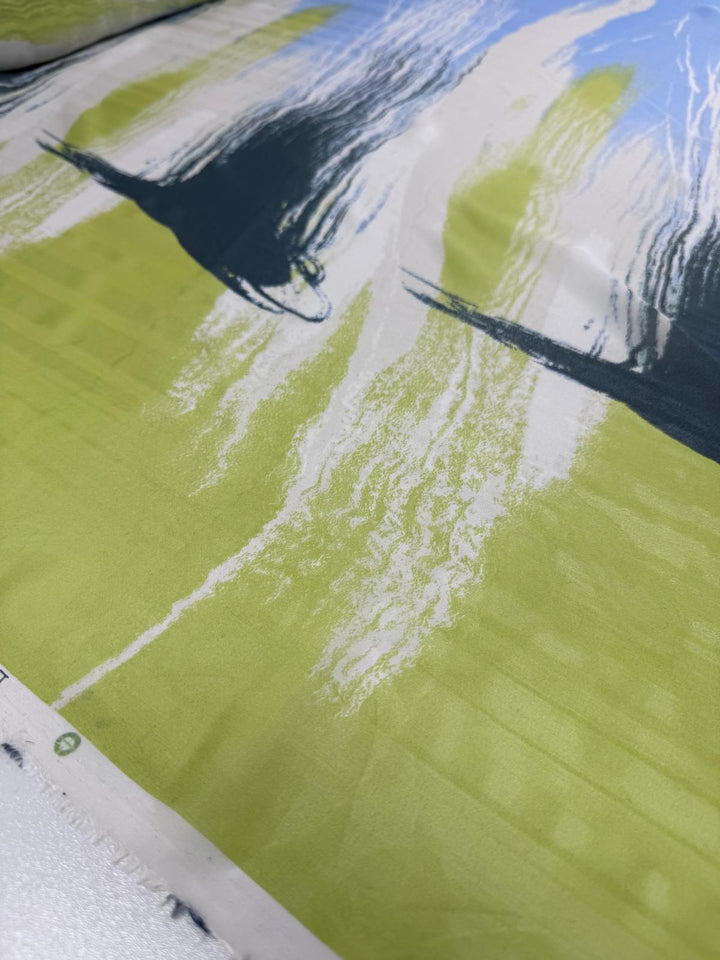 A close-up of the luxury fabric, Pure Silk - Speed - 112cm by Super Cheap Fabrics, showcases abstract patterns in green, white, and dark blue. Brush-like strokes create a dynamic textured appearance, perfect for high-end fashion. The pure printed silk is elegantly laid flat.