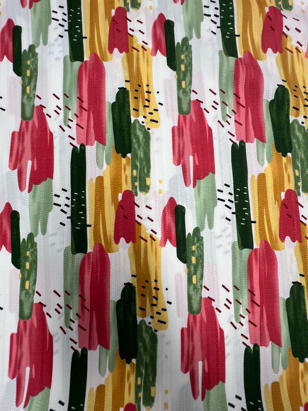 The Super Cheap Fabrics Textured Deluxe Print - Stroke & Speck 2.0 (155cm) is a vibrant polyester fabric with an abstract brushstroke pattern in red, green, yellow, and black on white, creating a lively and artistic look.