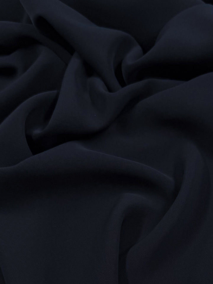 A close-up of the Super Cheap Fabrics' Microfibre Suiting in Dark Navy, 150cm wide, reveals its medium weight polyester fabric with gentle folds and a smooth, soft texture. The slightly reflective surface creates subtle highlights and shadows.
