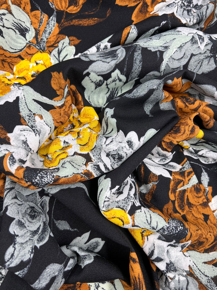 This is a close-up of the Printed Crepe - Marigoldine from Super Cheap Fabrics, featuring lightweight fabric with densely arranged abstract floral patterns in orange, yellow, gray, and white on a black background—ideal for vibrant high fashion designs. Width: 150cm.