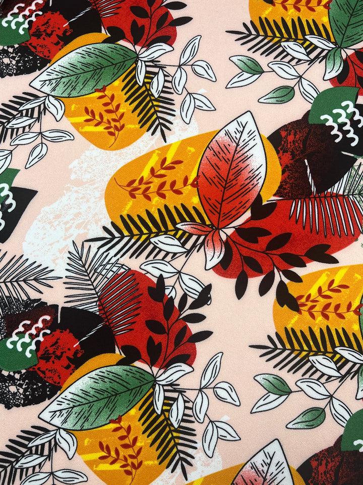 The Jungle Sunset Printed Crepe by Super Cheap Fabrics features a vibrant abstract pattern with overlapping leaves in red, green, and white on yellow, black, and orange shapes. This dynamic design offers a lively tropical feel with the luxurious touch of soft, lightweight 140cm fabric.