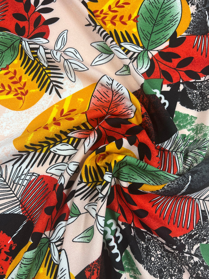 The Printed Crepe - Jungle Sunset by Super Cheap Fabrics features a luxurious pattern of large green, red, and yellow leaves with smaller white ones and abstract black, yellow, and red shapes. Lightweight and slightly gathered in the center, it adds a playful elegance to any design.